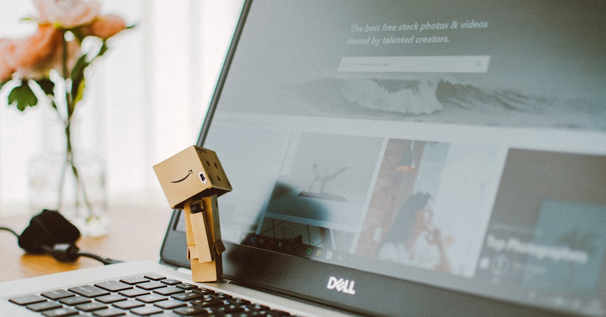 A small toy figure stands on a laptop keyboard with flowers in the background.