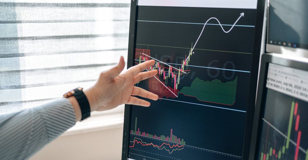 Close-up of a hand pointing at stock market graphs on a monitor in a workspace.