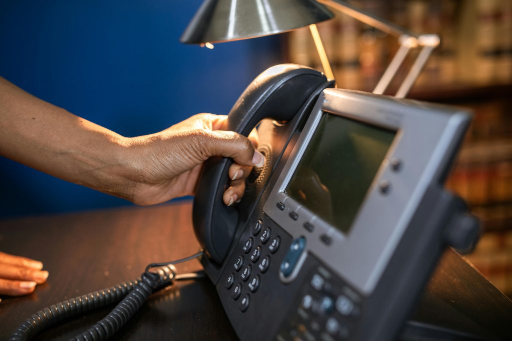 A close-up image of a hand picking up a handset from an office telephone, emphasizing communication device usage.